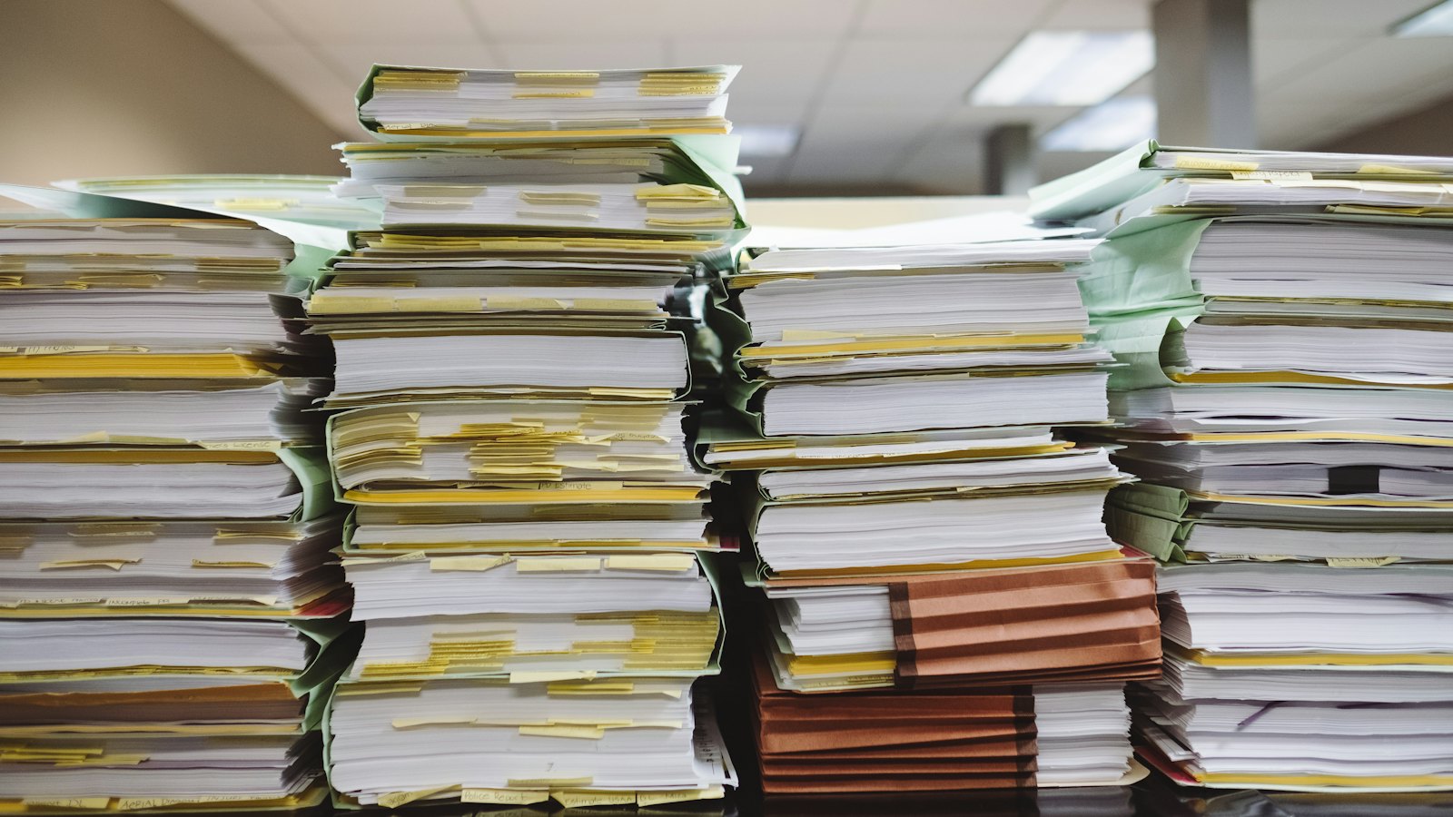 Pilhas altas de pastas e processos em papel sobre uma mesa de escritório
